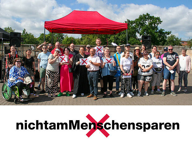 Sommerfest-Teilnehmende präsentieren das Motiv der bundesweiten Kampagne „Nicht am Menschen sparen“ Sommerfest-Teilnehmer mit Kampagnenmotiv „Nicht am Menschen sparen“