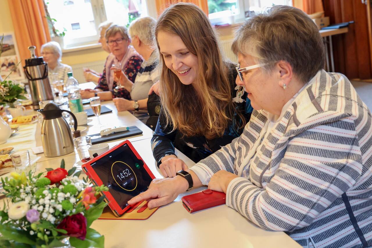 Junge Ehrenamtliche erklärt Seniorin Tablet-Funktionen